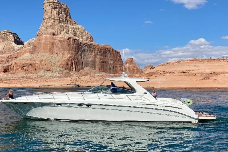 The Image of Sea Ray Sundancer 540 yacht cruising near rocky cliffs under a clear blue sky. - 0