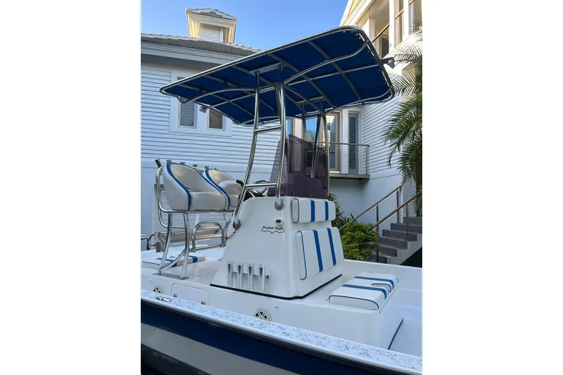Slide: The Image of 2018 Shallow Sport 24 Modified V boat with blue canopy and seating, docked near a house. - 2