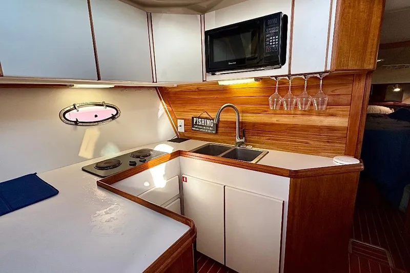 Slide: The Image of 1990 Tiara Yachts 3600 Open kitchen with stove, sink, microwave, and wooden cabinetry. - 6