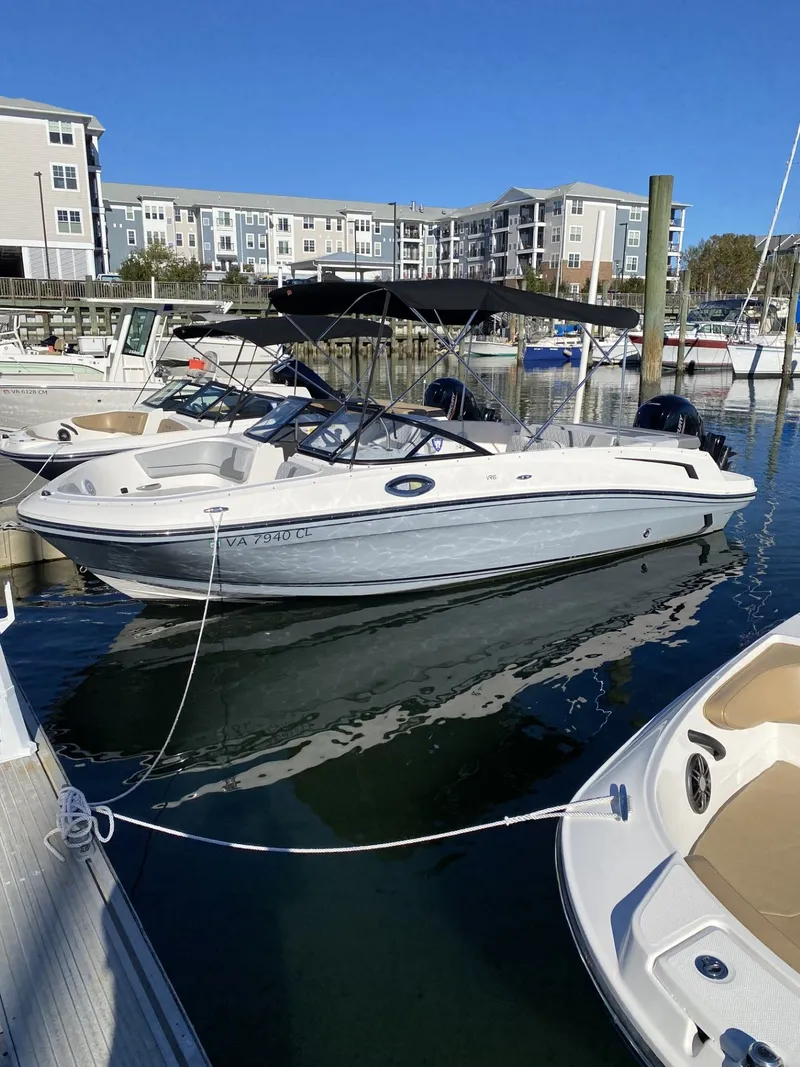 The Image of 2024 Bayliner VR6 boat docked in a marina with modern buildings in the background. - 0