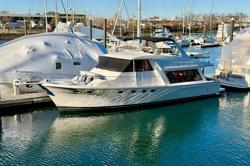 The Image of 1995 Bayliner 4788 Pilot House Motoryacht docked in a marina, surrounded by other boats. - 0
