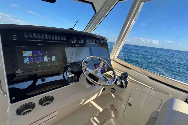 Slide: The Image of Boston Whaler 380 Realm 2022 helm with navigation screens, steering wheel, and ocean view. - 31