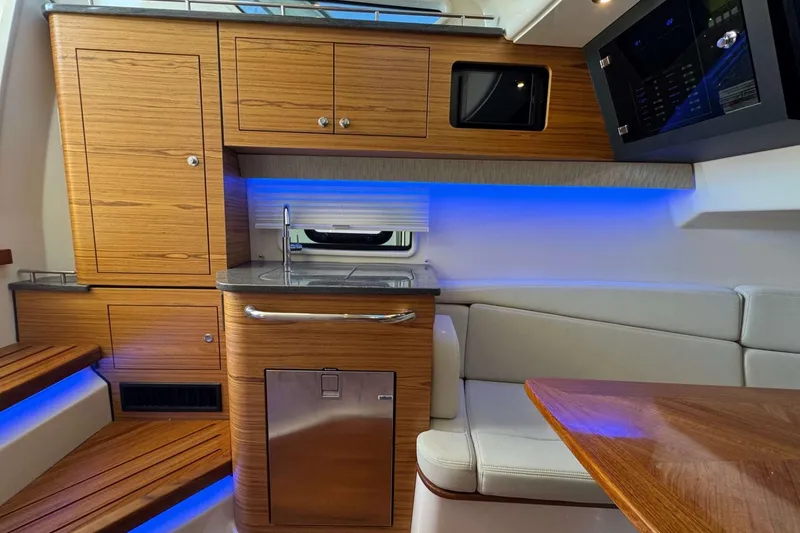 Slide: The Image of 2022 Boston Whaler 380 Realm interior with wood cabinetry, seating, and ambient blue lighting. - 39