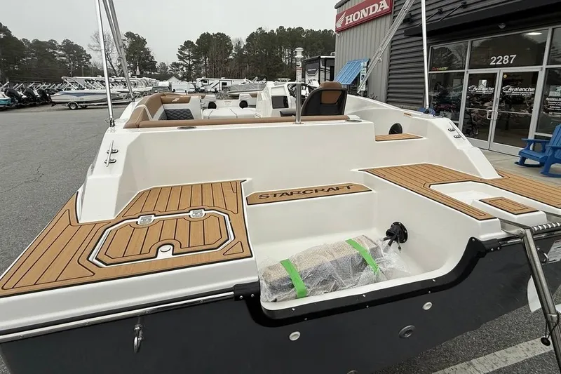 Slide: The Image of 2026 Starcraft SVX 191 OB boat with sleek design and wood accents, parked outside dealership. - 11
