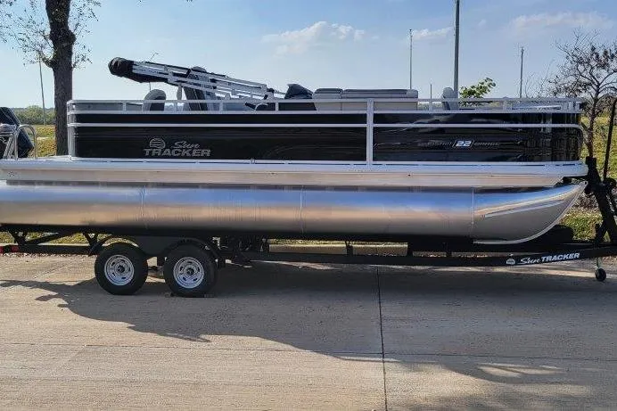 The Image of 2026 Sun Tracker Fishin' Barge 22 XP3 pontoon boat on trailer, parked outdoors. - 0