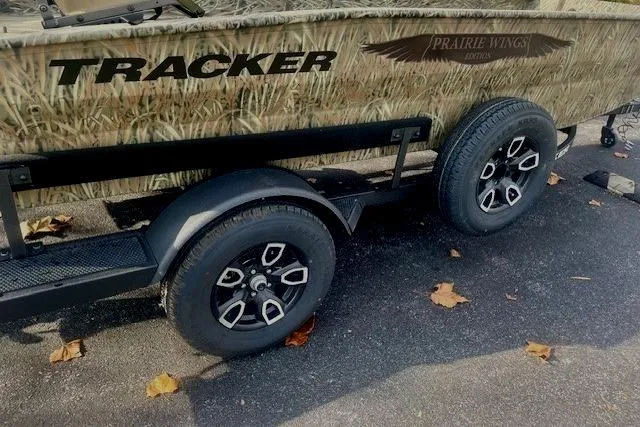Slide: The Image of 2026 Tracker Grizzly 1650 T Prairie Wings Edition boat trailer with camouflage design and black wheels. - 4