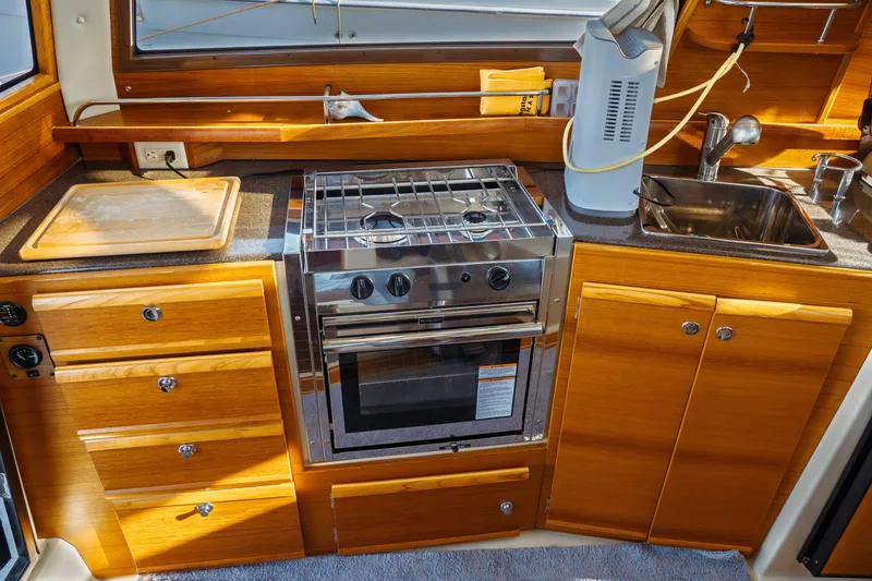 Slide: The Image of 2022 Ranger Tugs R-29 S galley with stove, sink, and wooden cabinetry. - 25