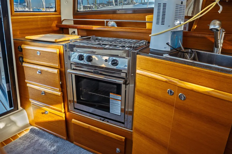 Slide: The Image of 2022 Ranger Tugs R-29 S galley with stove, wooden cabinetry, and sink. - 27
