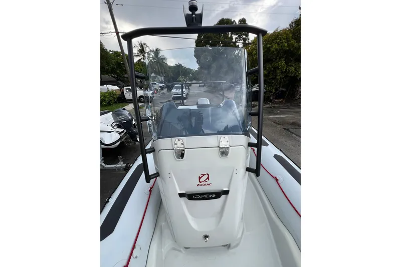 Slide: The Image of 2025 Zodiac Open 5.5 boat, front view with windshield and console, parked outdoors. - 5