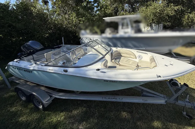 Slide: The Image of 2023 Key West 203 DFS boat on trailer, parked on grass, surrounded by trees. - 3