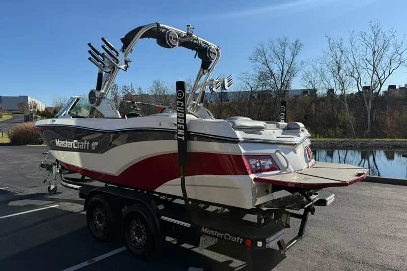 Slide: The Image of 2018 MasterCraft XT21 boat on trailer, parked near a lake under clear blue sky. - 5