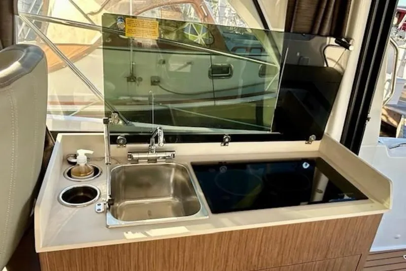 Slide: The Image of 2024 Beneteau Antares 9 boat kitchen with sink, glass cover, and wooden cabinetry. - 8
