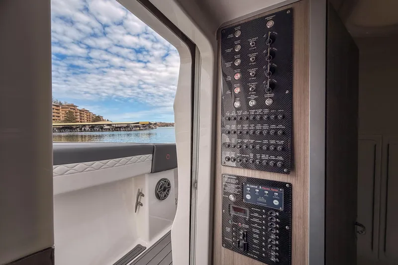 Slide: The Image of 2020 Fountain 43 NX boat interior with control panels, overlooking a scenic waterfront view. - 55