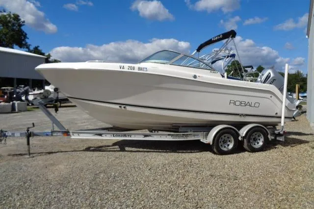 The Image of 2005 Robalo R227 Dual Console boat on trailer, parked outdoors under blue sky. - 1