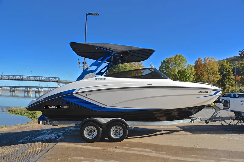 Slide: The Image of 2018 Yamaha Boats 242X on trailer by river, clear blue sky background. - 15