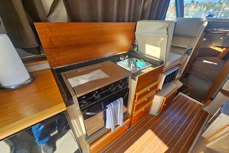Slide: The Image of 2015 Cutwater 30 Command Bridge interior kitchen with stove, sink, and wooden cabinetry. - 31