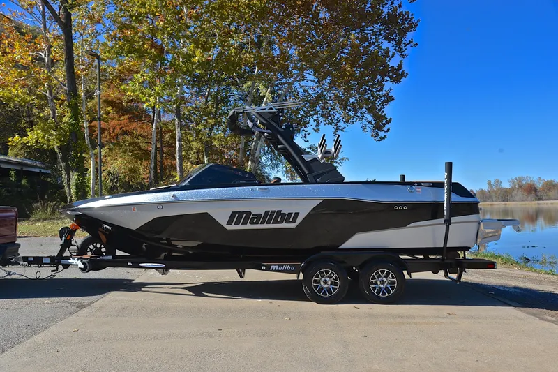 Slide: The Image of 2023 Malibu Wakesetter 23 LSV boat on trailer by a lake, surrounded by autumn trees. - 11