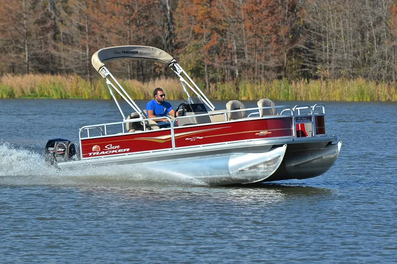 The Image of 2023 Sun Tracker Bass Buggy 18 DLX pontoon boat cruising on a serene lake. - 1