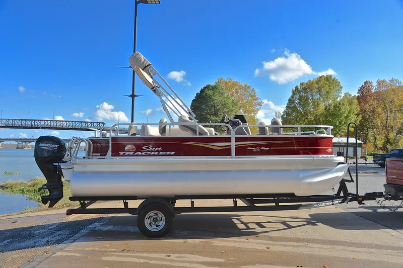 Slide: The Image of 2023 Sun Tracker Bass Buggy 18 DLX pontoon boat on trailer by a river. - 15
