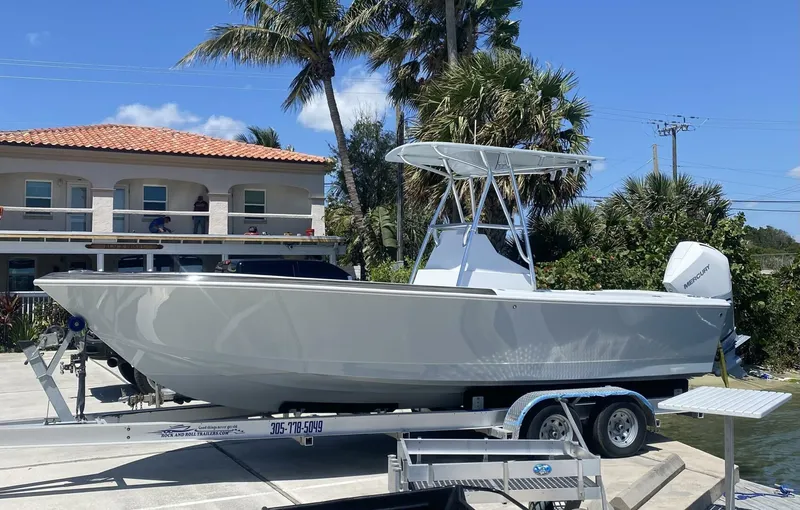 Slide: The Image of 1988 Intrepid 24 boat on trailer, parked near waterfront with palm trees and building in background. - 9