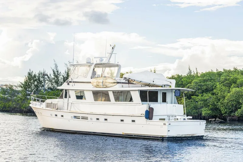 Slide: The Image of 1987 Hatteras 70 Cockpit Motor Yacht on calm water, surrounded by lush greenery. - 40