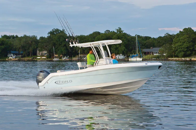 The Image of 2026 Robalo R222 Center Console boat on trailer, blue and white design, parked outdoors. - 0