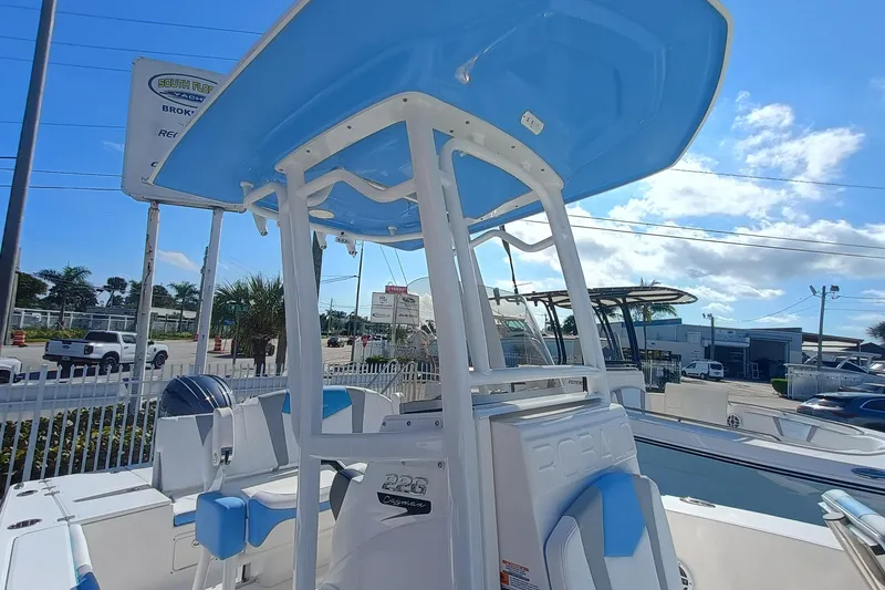 Slide: The Image of 2026 Robalo 226 Cayman boat with blue T-top, parked outdoors under clear sky. - 19