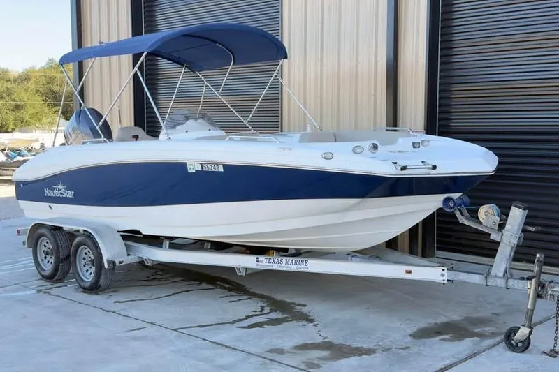 Slide: The Image of 2013 NauticStar 203 SC boat on trailer with blue canopy, parked outside a building. - 2