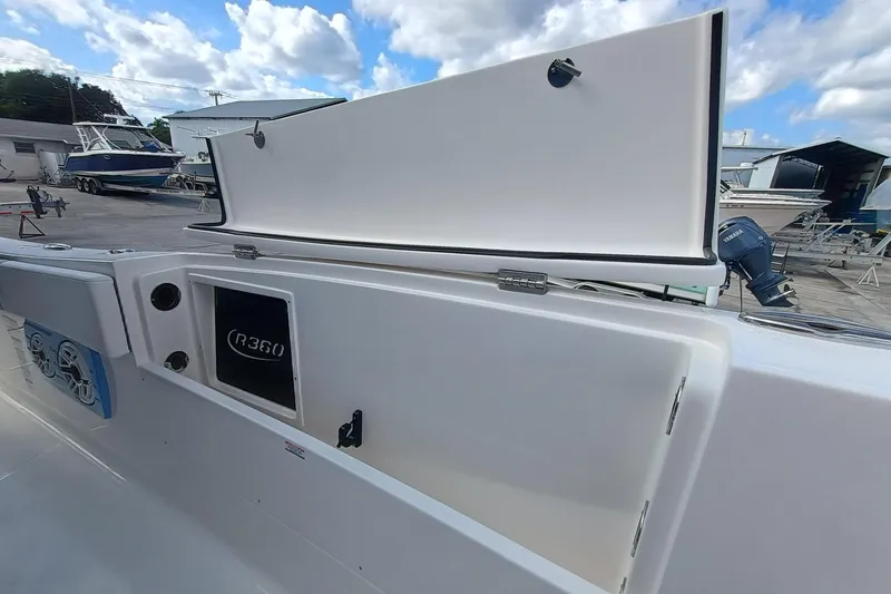 Slide: The Image of 2026 Robalo R360 Center Console boat with open storage compartment, docked under cloudy sky. - 29