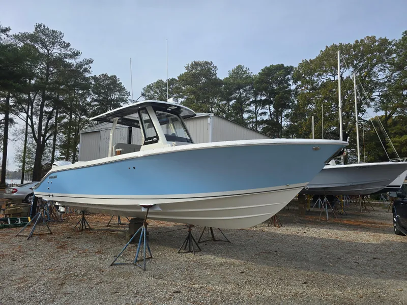 The Image of 2025 Pursuit S 288 boat in a yard, elevated on stands, surrounded by trees. - 0