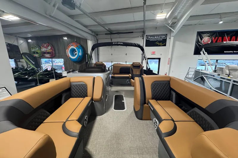 Slide: The Image of 2026 Sylvan L3 DLZ pontoon boat interior with tan and black seating in showroom. - 10