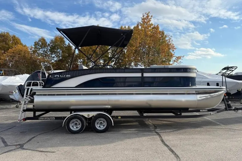 Slide: The Image of 2026 Lowe SS 230 DV pontoon boat on trailer, parked outdoors under blue sky. - 4