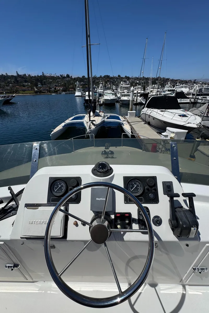 Slide: The Image of 2001 Zeta Flybridge Power Catamaran helm with marina view, clear skies, and docked boats. - 42