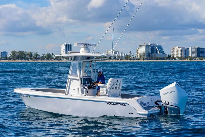 Slide: The Image of 2024 Reef Runner 230 Open boat cruising near a city shoreline. - 49