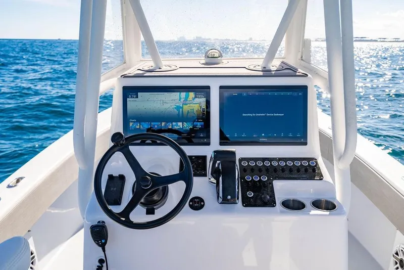 Slide: The Image of 2024 Reef Runner 230 Open boat dashboard with dual screens and steering wheel on open water. - 57