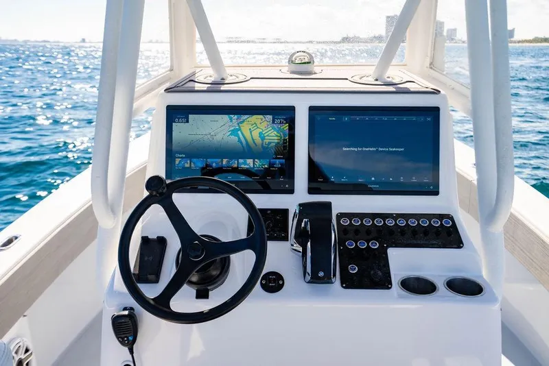 Slide: The Image of 2024 Reef Runner 230 Open boat dashboard with dual screens and steering wheel on open water. - 60