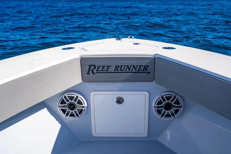 Slide: The Image of 2024 Reef Runner 230 Open boat bow with speakers, on blue ocean water. - 72