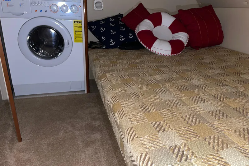 Slide: The Image of Laundry area and cozy bed with nautical-themed pillows on a 2004 Carver 460 Voyager. - 22