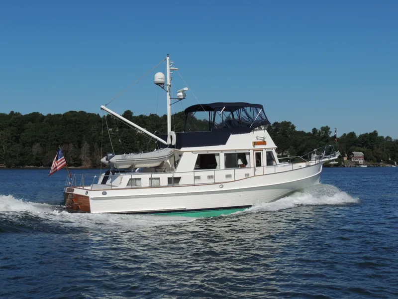 Slide: The Image of 2002 Grand Banks 42 Classic yacht cruising on a sunny day, with lush greenery in the background. - 4