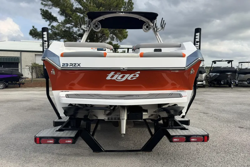 Slide: The Image of 2021 Tigé 23RZX boat, rear view, orange and white design, parked outdoors. - 3