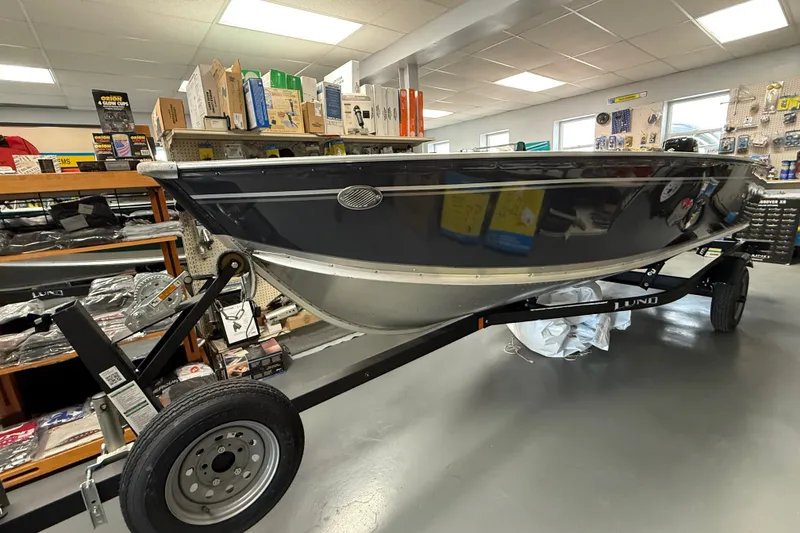 The Image of 2026 Lund Fury 1600 Tiller boat on trailer in showroom, surrounded by boating accessories. - 0