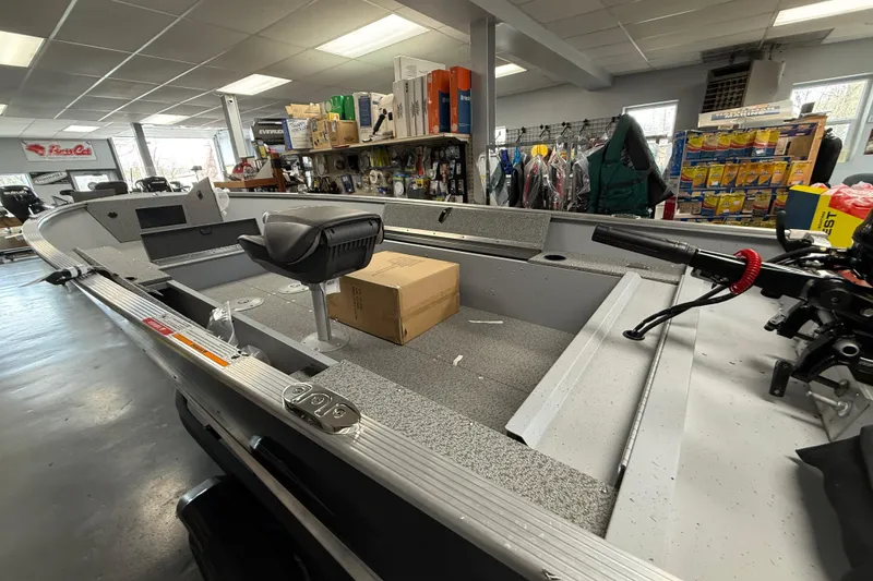 Slide: The Image of 2026 Lund Fury 1600 Tiller boat interior in showroom, featuring seating and storage. - 2