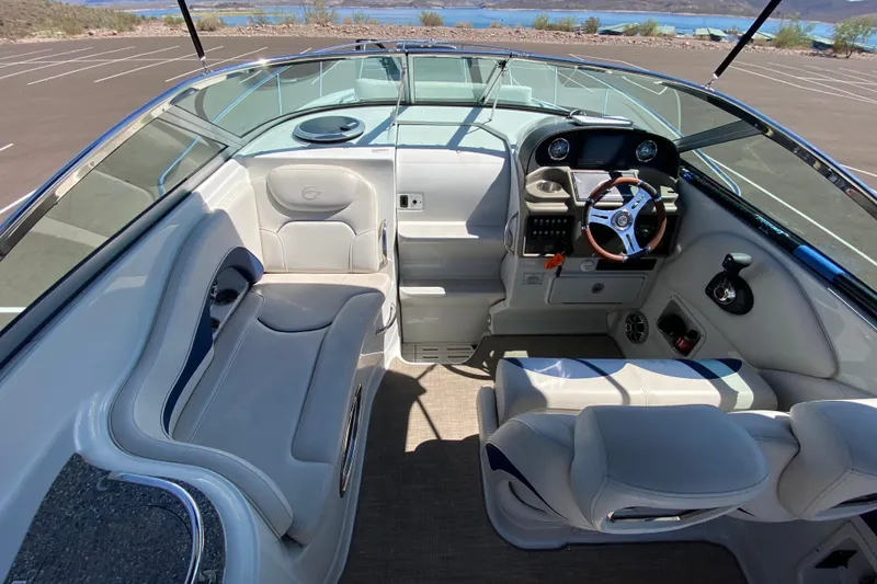 Slide: The Image of 2022 Crownline 264 CR boat interior with steering wheel and seating, parked near a lake. - 48