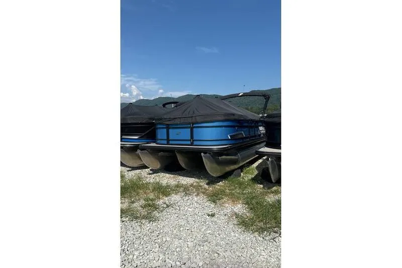 Slide: The Image of 2024 Starcraft EXS 3 pontoon boat with blue exterior, covered and parked outdoors. - 3