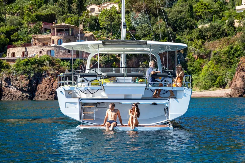 Slide: The Image of 2026 Hanse 590 yacht anchored near scenic coastal villas, with people enjoying the water. - 24