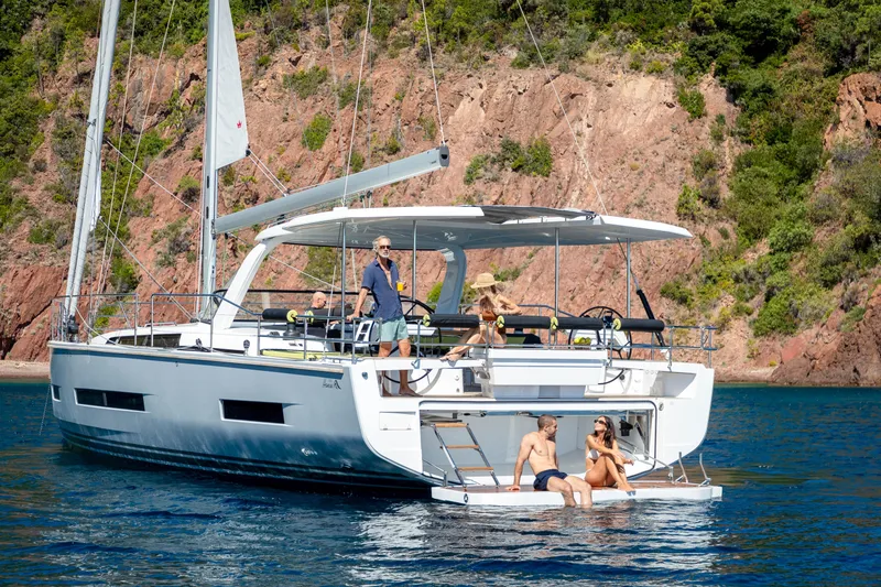 Slide: The Image of 2026 Hanse 590 yacht anchored near rocky coastline with people relaxing on deck. - 2
