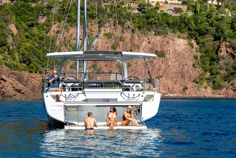 Slide: The Image of 2026 Hanse 590 yacht with people relaxing, anchored near a rocky coastline. - 3