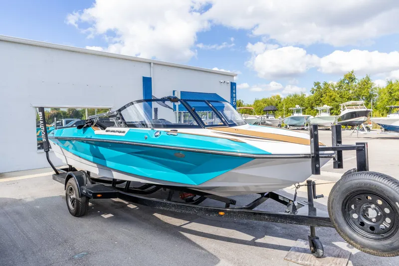 The Image of 2023 Nautique Ski Nautique boat on trailer, vibrant blue and white design, outdoor dealership setting. - 0