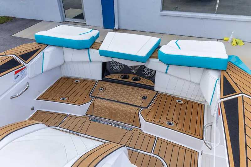Slide: The Image of 2023 Nautique Ski Nautique boat interior with teak flooring and white-blue cushioned seating. - 8