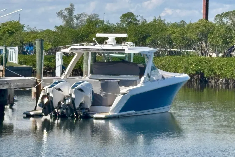 Slide: The Image of 2019 Tiara Sport 38 LS boat docked in calm waters, surrounded by greenery. - 34